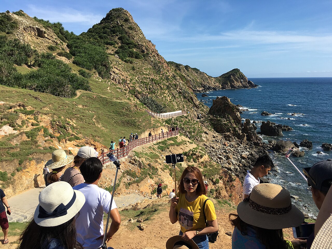 Visiteurs sur le sentier en pente d'Eo Gió, rochers et mer au fond