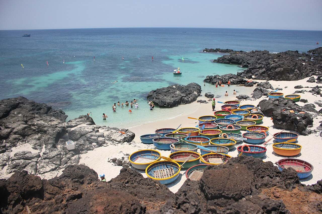 Plage de rochers noirs et eau turquoise de l'île de Bé, à Lý Sơn, avec des bateaux-paniers
