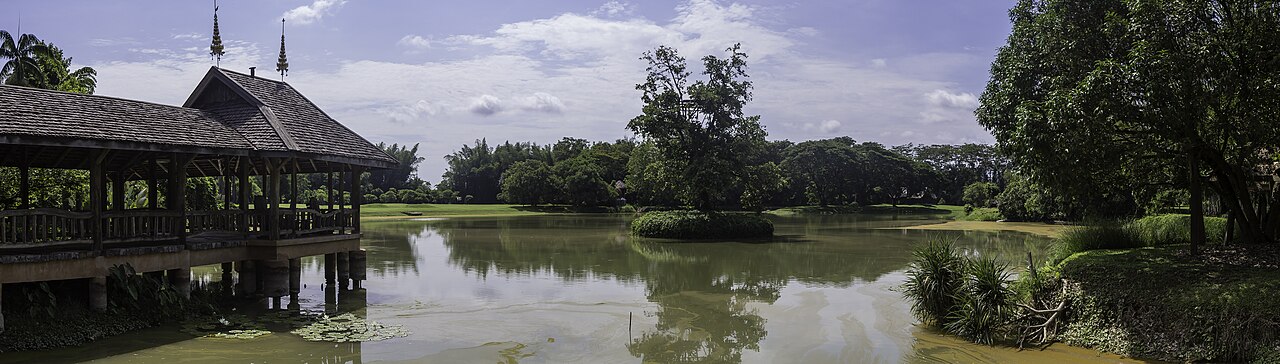 Pavillon de bois sur pilotis et étang du parc Mae Fah Luang sous un ciel bleu