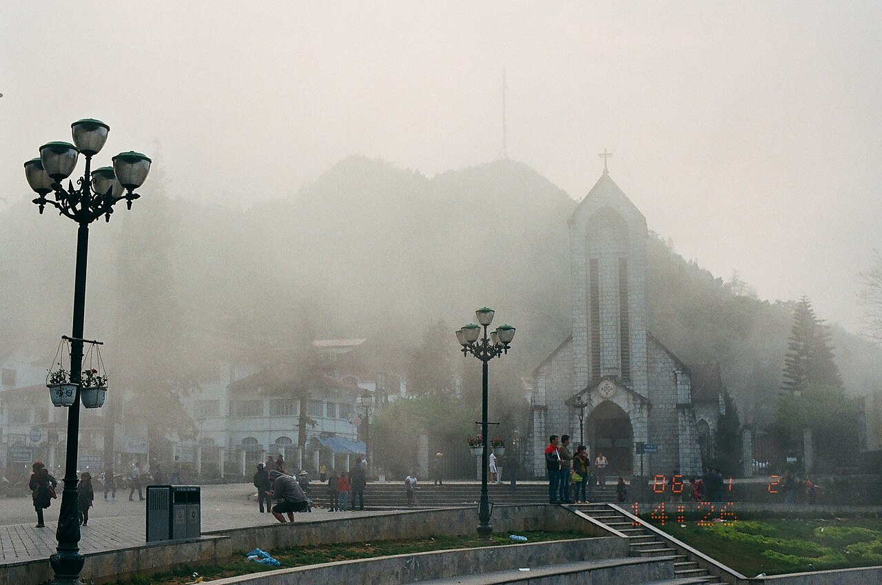 Église en pierre de Sa Pa à demi cachée par la brume et lampadaires de la place